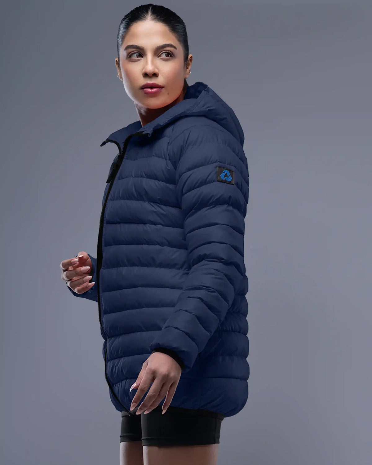 Woman wearing a navy blue puffer jacket on a gray background