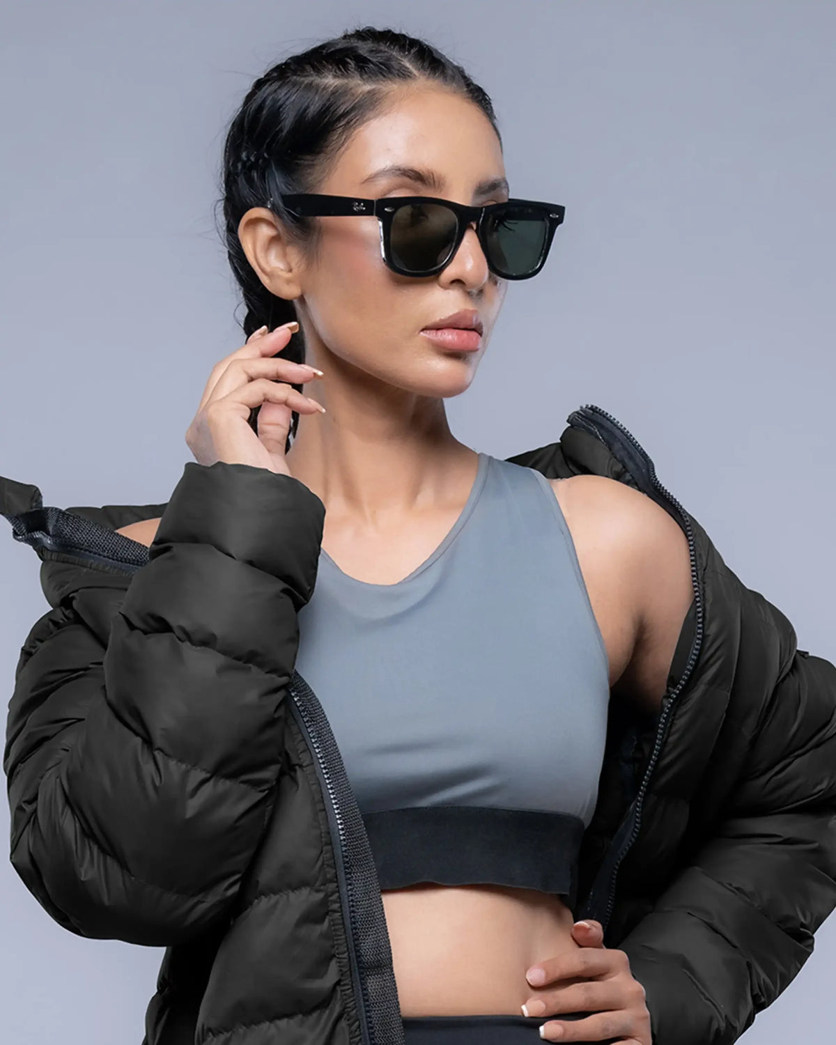 Woman wearing a black puffer jacket and gray sports bra against a gray background