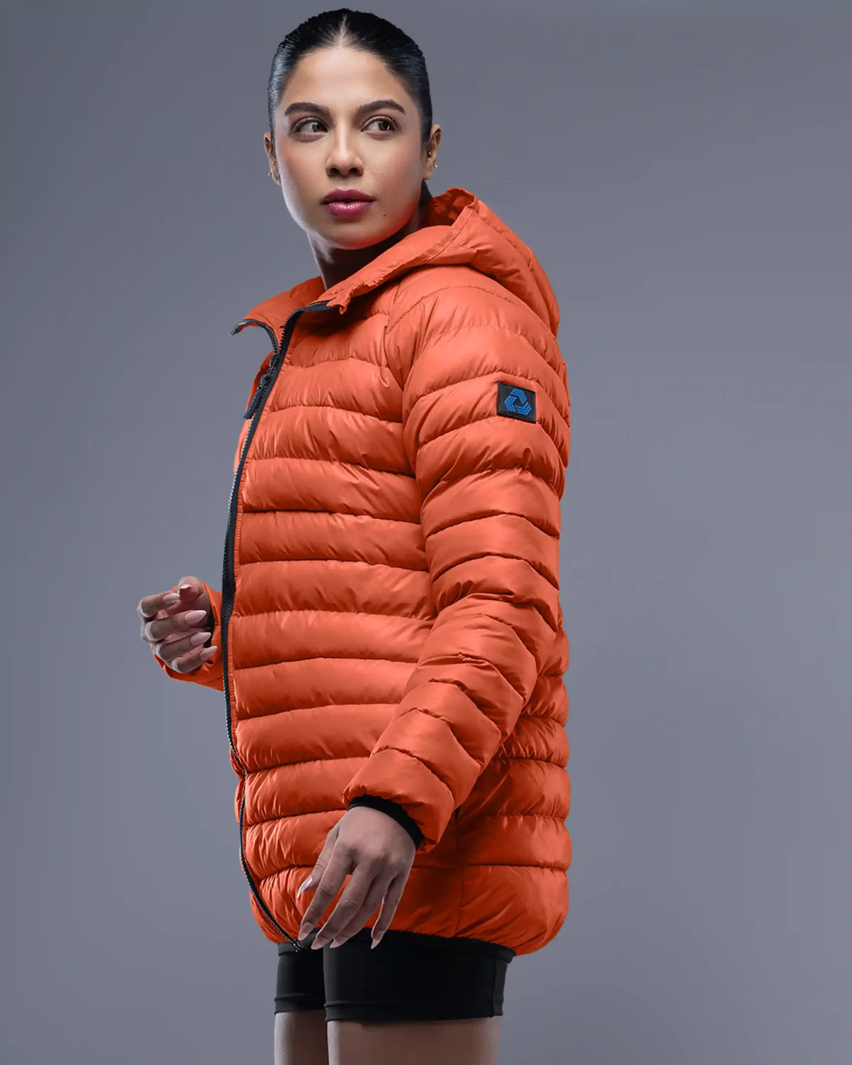 Person wearing an orange puffer jacket on a gray background