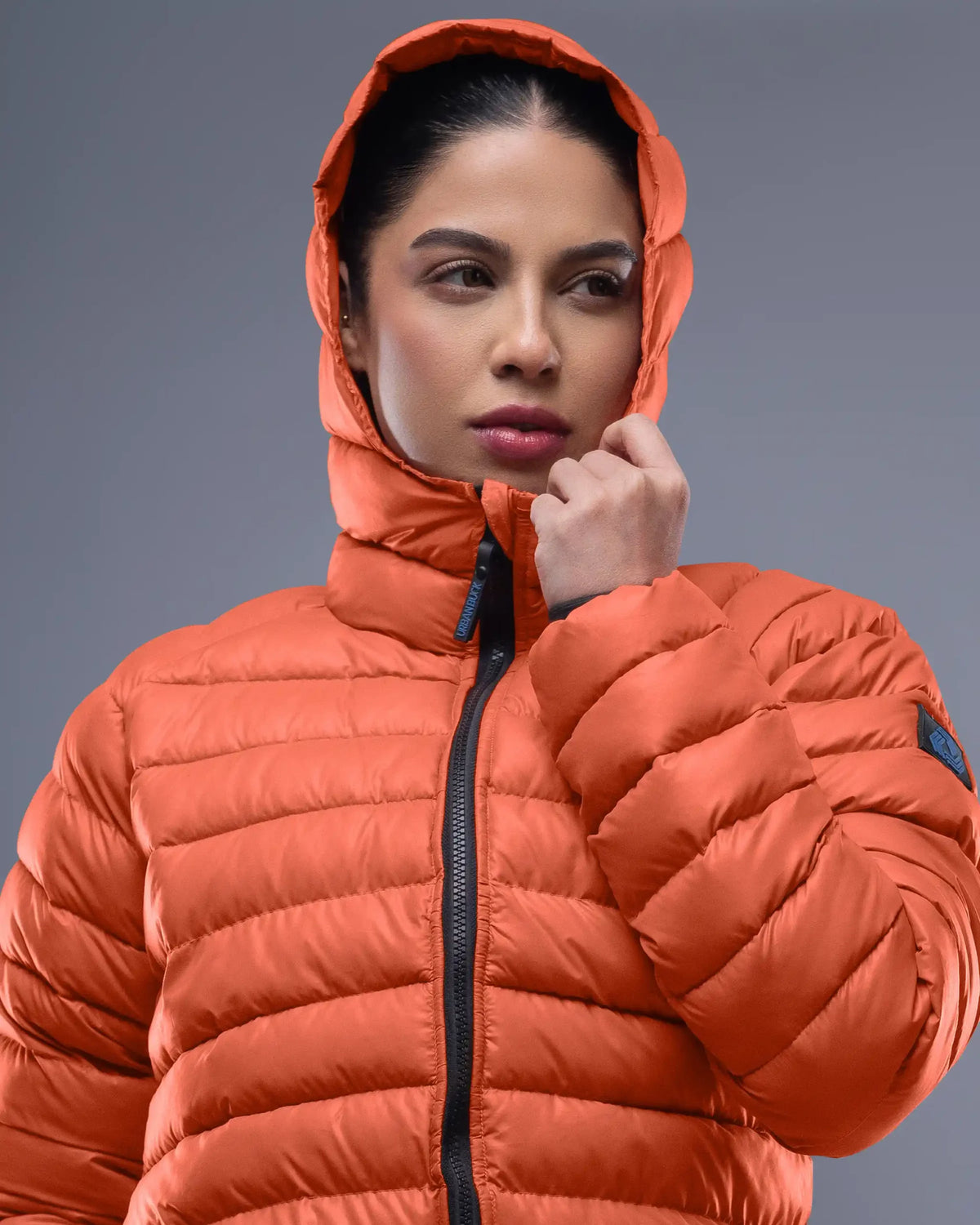 Person wearing an orange puffer jacket against a gray background