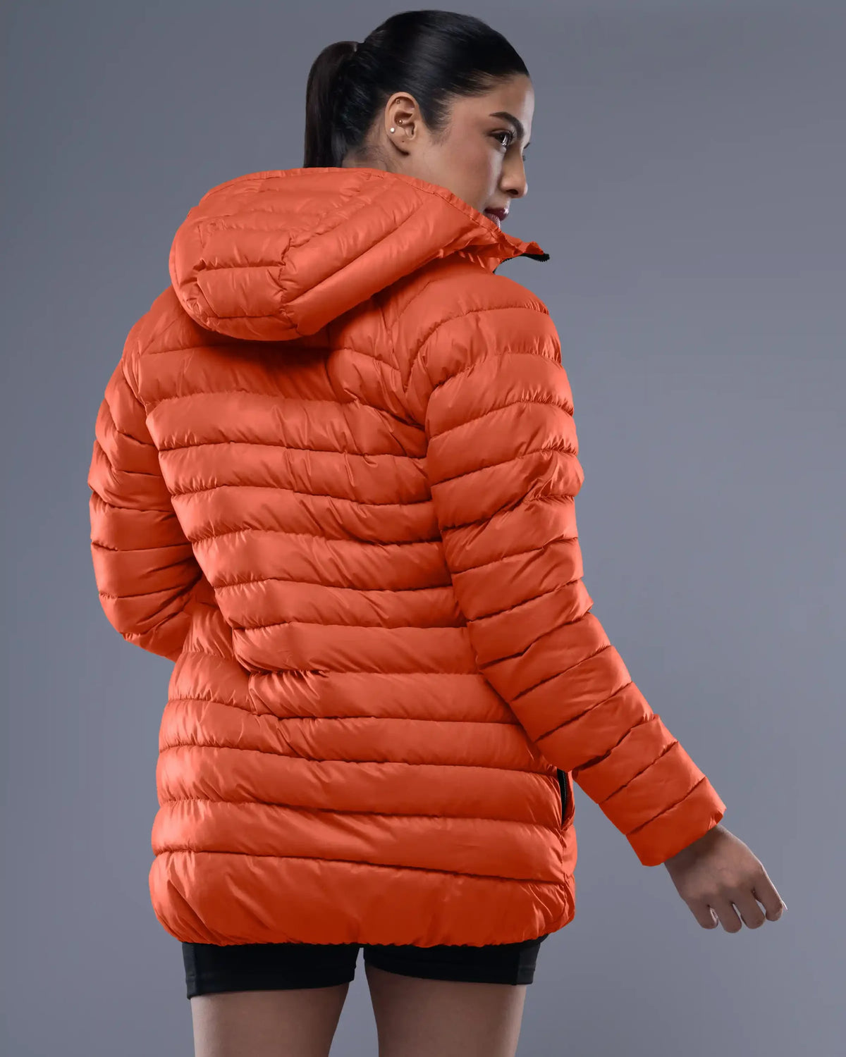 Person wearing an orange puffer jacket on a gray background