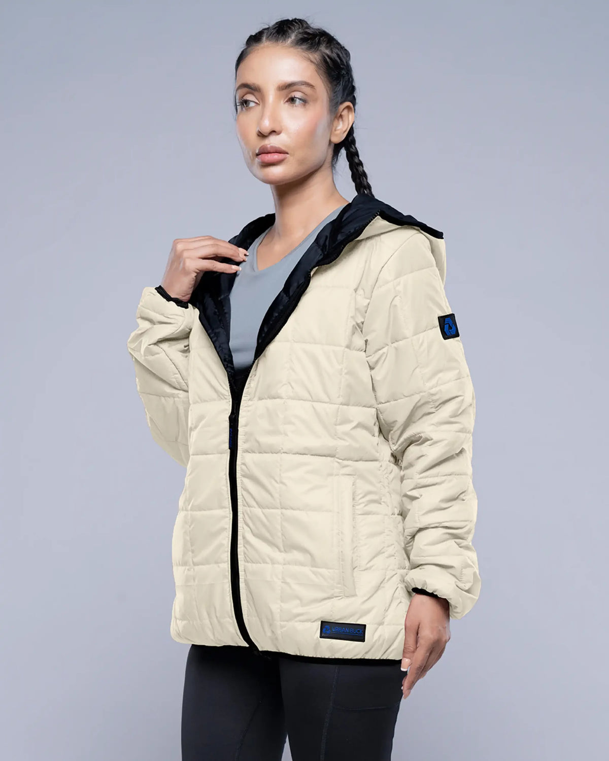 Woman wearing a beige quilted jacket with black accents on a gray background