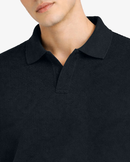 Close-up of a person wearing a black polo shirt with a plain background