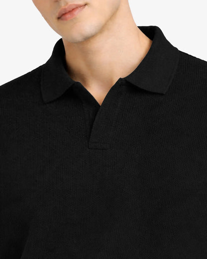 Close-up of a person wearing a black polo shirt with a plain background