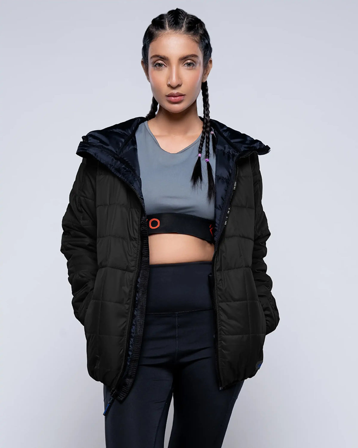 Woman wearing a black puffer jacket over athletic wear on a light gray background