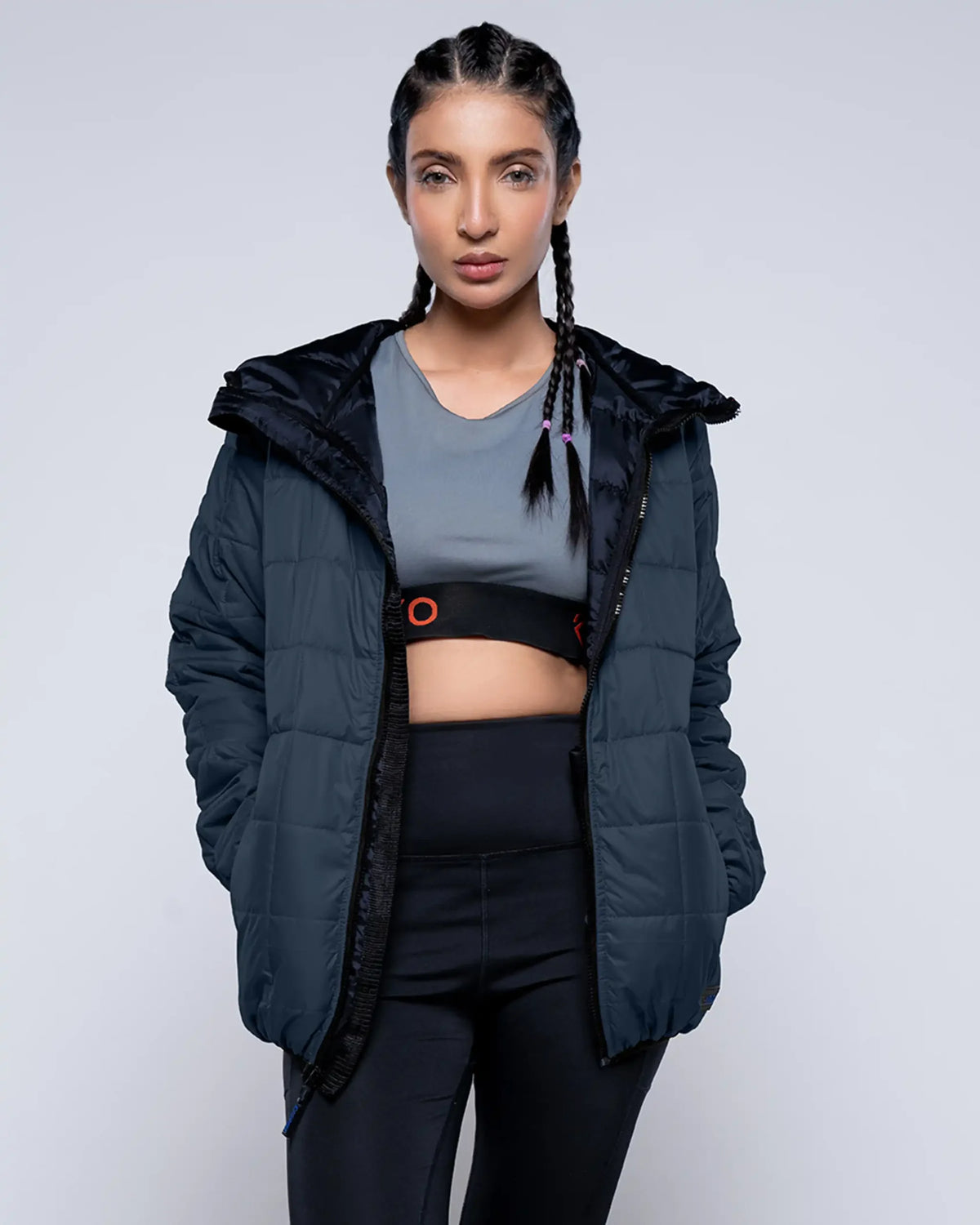 Woman wearing a black puffer jacket over athletic wear on a light gray background