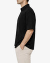 Man wearing a black short-sleeve shirt and beige pants on a white background