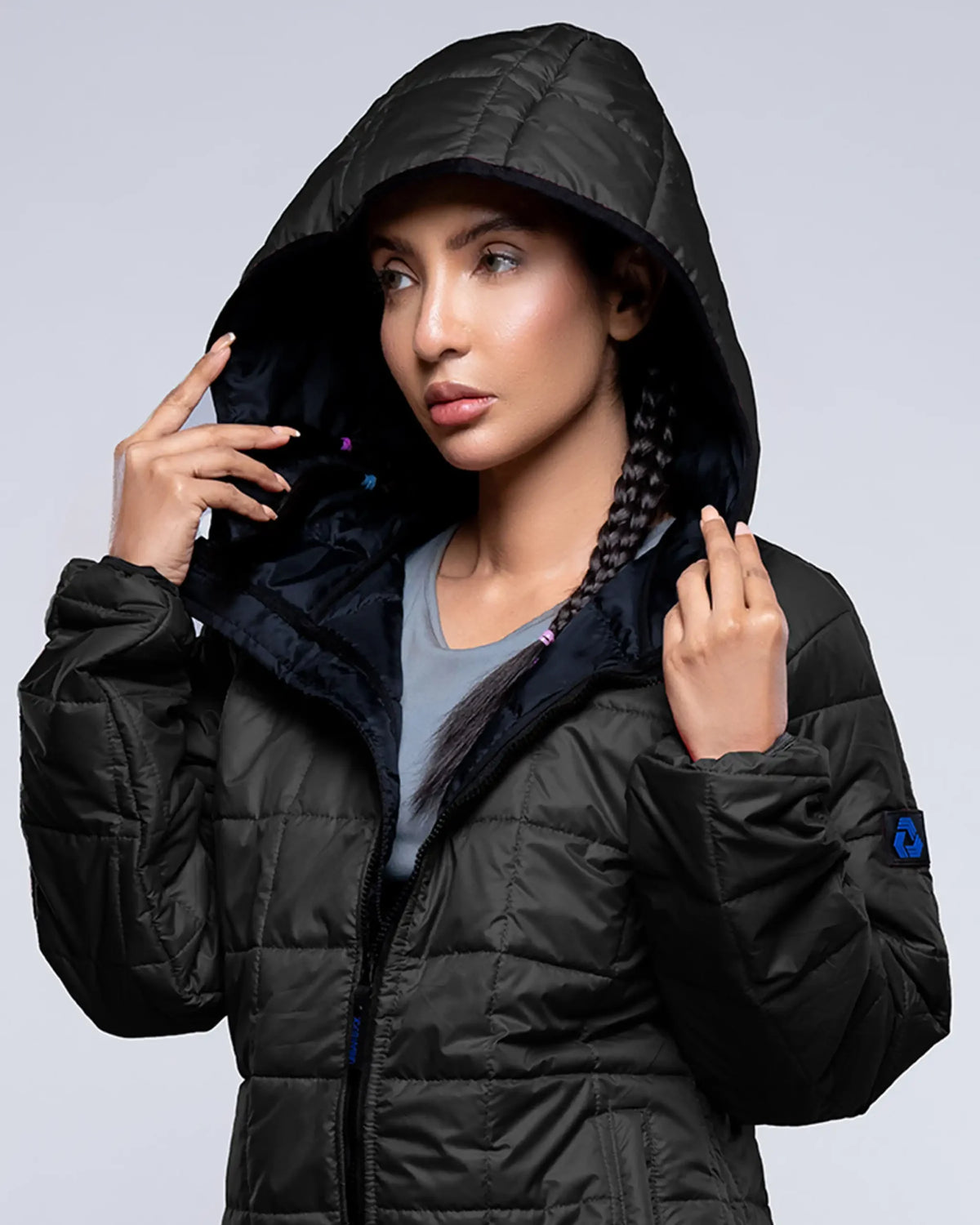 Person wearing a black puffer jacket with a hood against a gray background