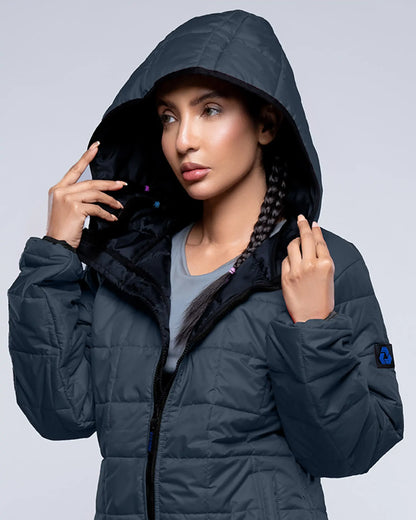 Woman wearing a dark blue puffer jacket with a hood against a light gray background