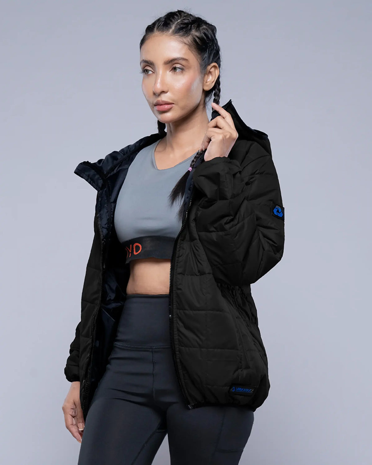 Woman wearing a black jacket and gray sports bra with black leggings on a gray background