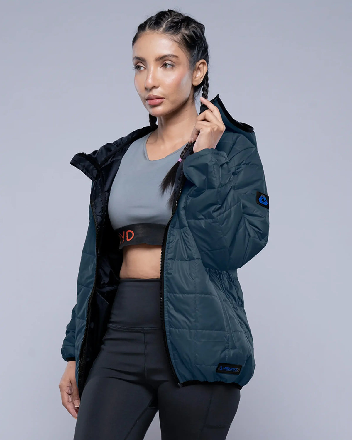 Woman wearing a dark green jacket over athletic wear on a gray background