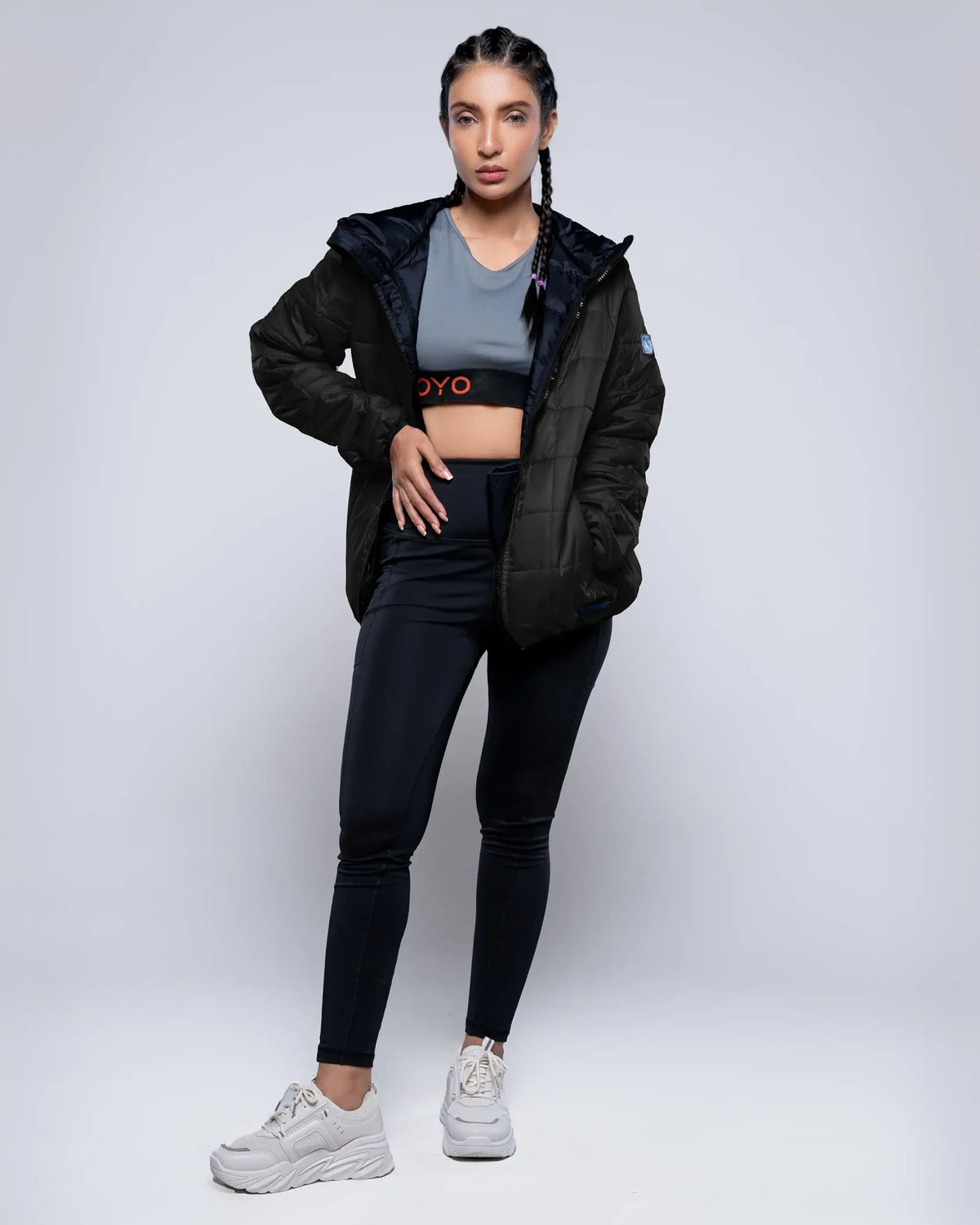 Woman wearing a black jacket, gray top, and black leggings on a white background