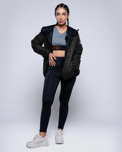Woman wearing a black jacket, gray top, and black leggings on a white background