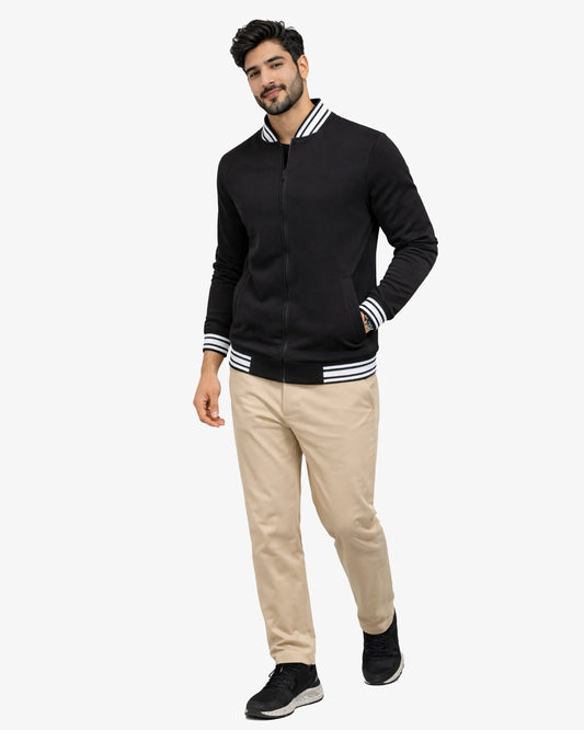 Man wearing a black bomber jacket with white stripes and beige pants on a white background
