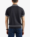 Person wearing a black polo shirt with white trim on a plain background