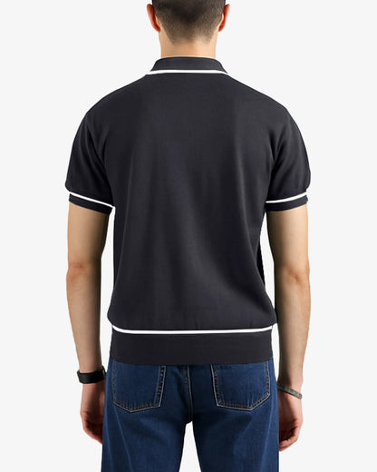 Person wearing a black polo shirt with white trim on a plain background