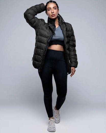 Person wearing a black puffer jacket, black leggings, and gray sneakers on a light gray background
