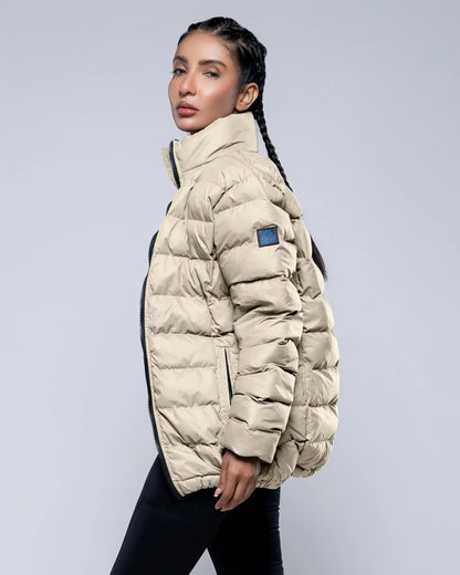 Woman wearing a beige puffer jacket with a blue patch on a light gray background