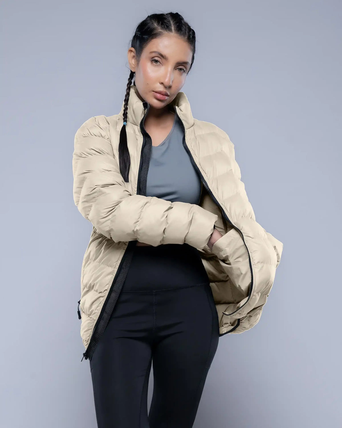 Woman wearing a beige puffer jacket over athletic wear on a gray background