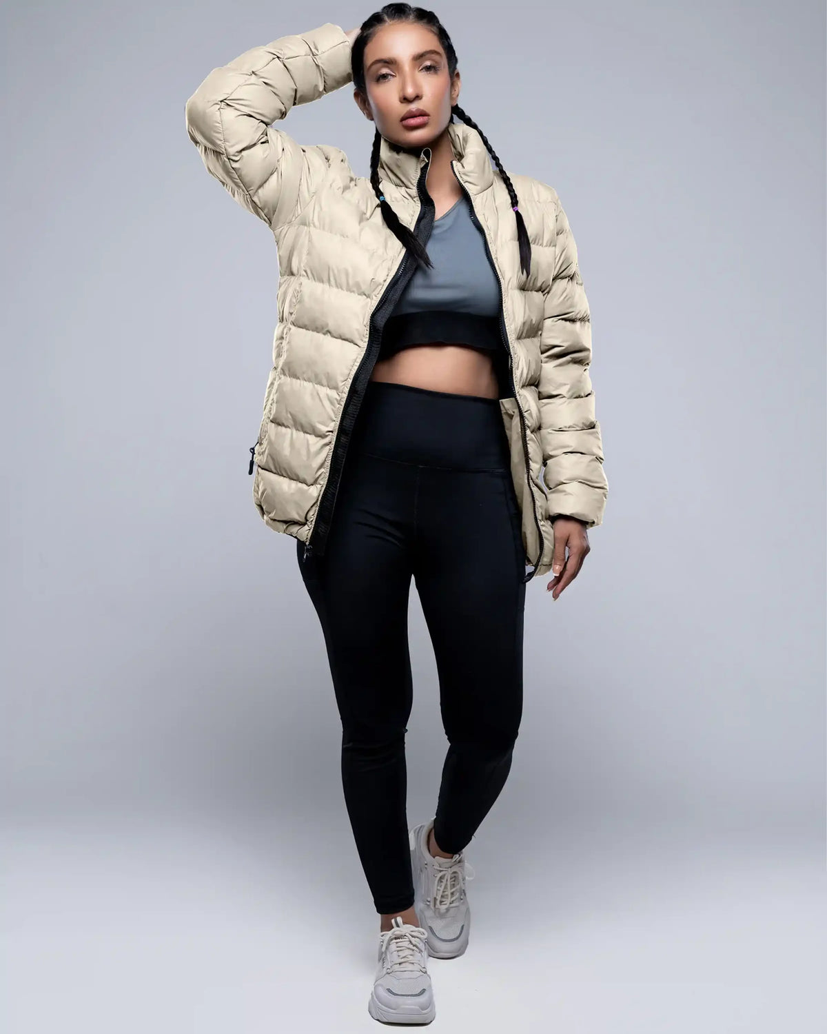 Person wearing a beige puffer jacket, black leggings, and gray sneakers on a light gray background