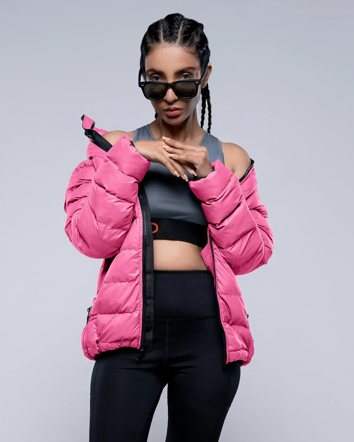 Person wearing a pink puffer jacket and black athletic outfit on a gray background