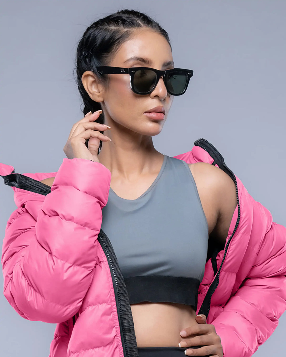 Woman wearing a pink puffer jacket and gray sports bra against a gray background