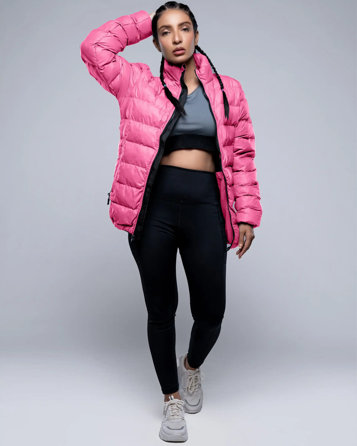 Person wearing a pink puffer jacket, black leggings, and gray sneakers on a gray background