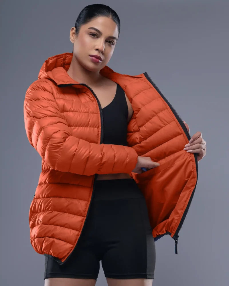 Woman wearing an orange puffer jacket against a gray background