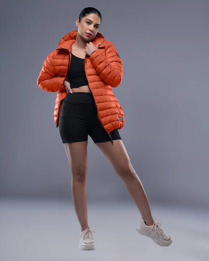 Person wearing an orange puffer jacket, black top, and shorts on a gray background